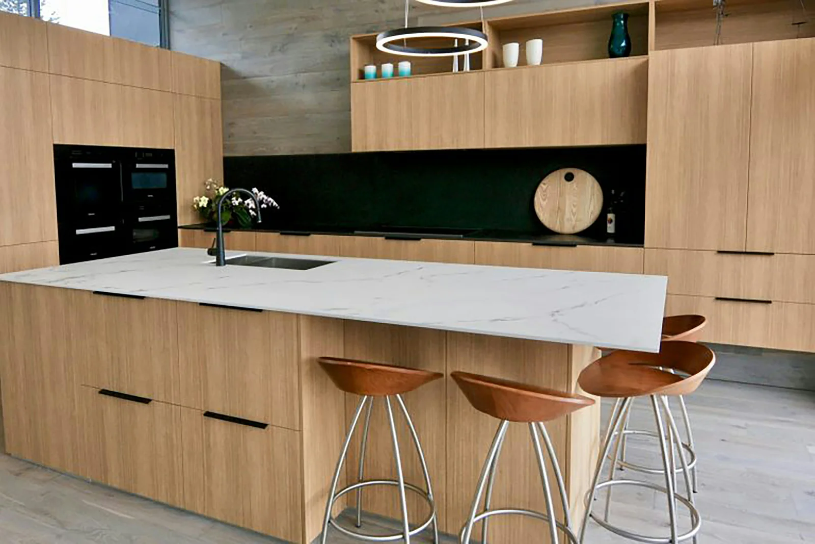 Keuken in licht eiken met een wit eiland en lederen barkrukken