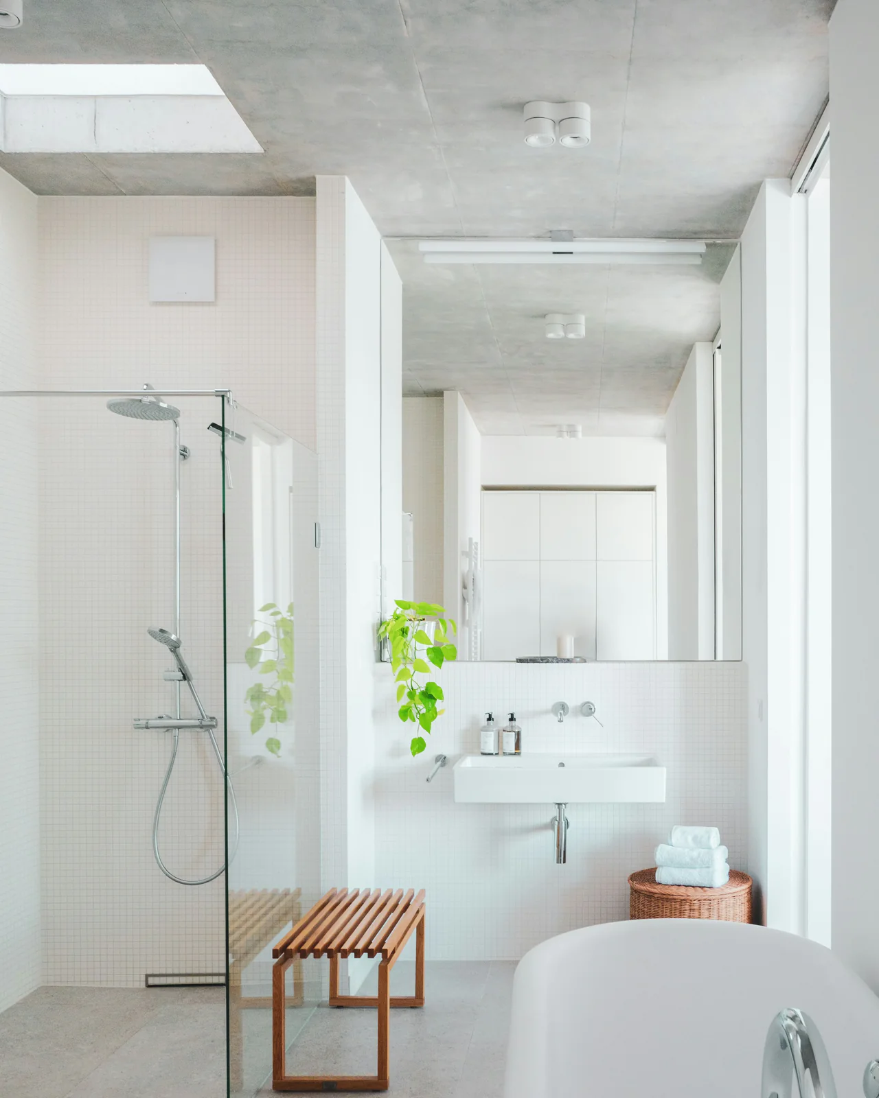 Witte badkamer met inloopdouche, wandlavabo en een houten bankje