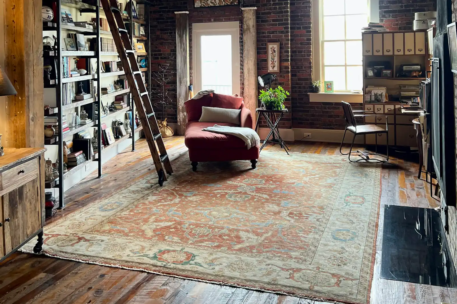 Loft met bakstenen muren, een boekenwand met ladder en een rood ligbed