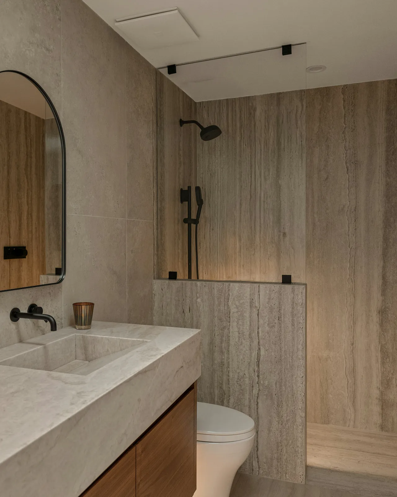 Badkamer in travertin met een stenen wastafel en een notelaren meubel